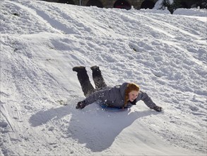 Caucasian teenage girl sledding on snowy hill