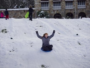 Caucasian teenage girl sledding on snowy hill