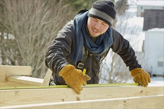 Caucasian carpenter measuring wood planks in winter