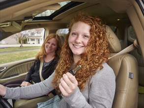 Caucasian teenage girl showing key with mother in car