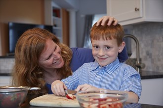 Caucasian mother and son chopping fruit in kitchen