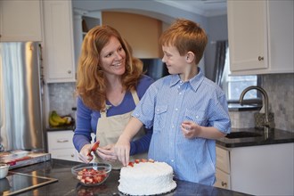 Caucasian mother and son decorating cake in kitchen