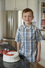 Caucasian boy standing with cake in kitchen