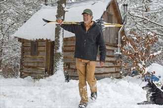 Mixed race man carrying skis near snowy shed