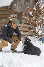 Mixed race man petting dog in snow