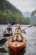 Caucasian couple paddling kayaks in remote river