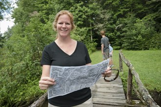 Caucasian woman reading map on footbridge in forest