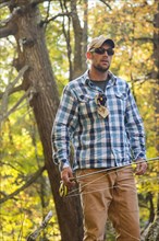 Caucasian man carrying fishing rod under tree