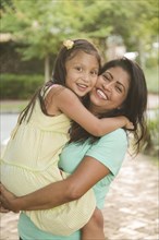 Hispanic mother carrying and hugging daughter