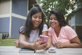 Hispanic mother and daughter texting on cell phone near apartments