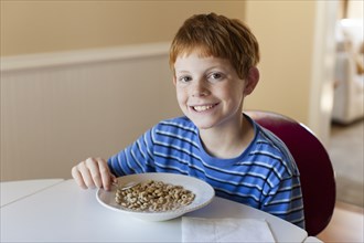 Smiling Caucasian boy eating cereal for breakfast