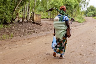 Mother carrying baby with traditional wrap on dirt road