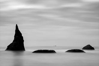 Fog over rock formations in ocean under cloudy sky