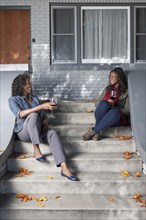 Black mother and daughter sitting on front stoop drinking wine