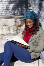 Black woman reading book on front stoop
