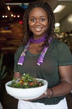 Black waitress serving salad in restaurant