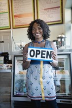 Black woman holding open sign in bakery