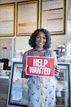 Black woman holding help wanted sign in bakery