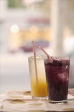 Orange and grape juice in glasses with straws