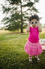 Black baby girl putting on sunglasses in park