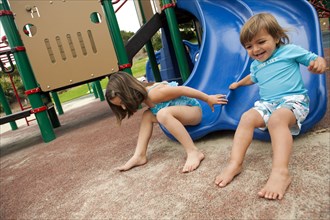 Brother and sister sliding down slide on playground