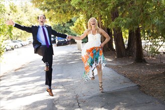 Caucasian newlywed couple skipping on road