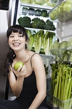 Mixed race woman with apple near green vegetables in refrigerator