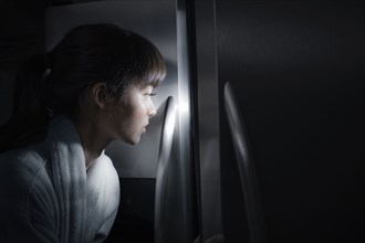 Mixed race woman peering into refrigerator at night