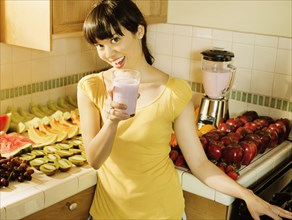Mixed race woman drinking smoothie in kitchen