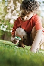 Caucasian boy looking at grass with magnifying glass