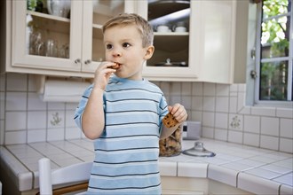 Caucasian boy eating cookie in kitchen