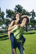 Teenager carrying girlfriend on his back in park