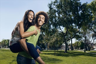 Teenager carrying girlfriend on his back in park