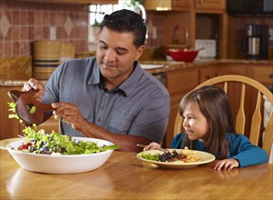 Father serving daughter salad at dinner table