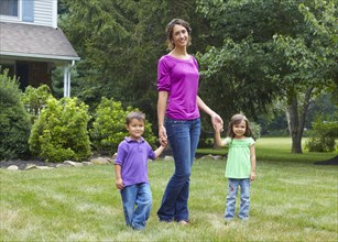 Mother holding hands with son and daughter in front yard