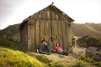 Couple sitting against barn in rural landscape