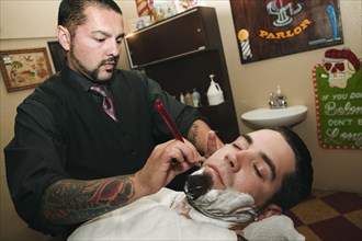 Hispanic barber shaving man's face