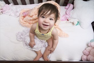 Mixed race baby girl sitting in crib