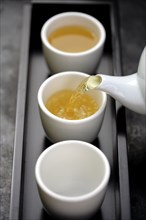 Green tea being poured from teapot into cups on tray