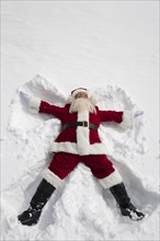 Santa Claus making snow angel outdoors