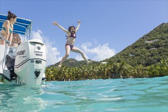Caucasian woman jumping off boat in tropical ocean