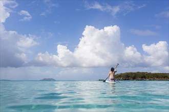 Caucasian woman paddling surfboard on tropical ocean