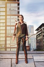 Mixed race woman with bow and arrow on urban rooftop