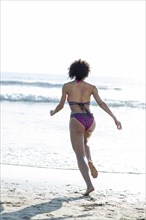 Mixed Race woman wearing bikini running to ocean