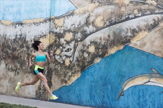 Mixed Race woman running on sidewalk near mural