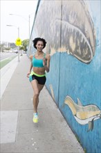 Mixed Race woman running on sidewalk near mural