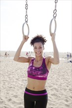Mixed Race woman holding gymnastics rings at beach