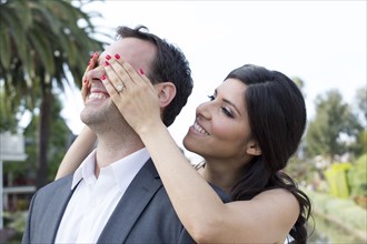 Woman standing behind man covering his eyes