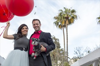 Smiling couple holding dog and red balloons