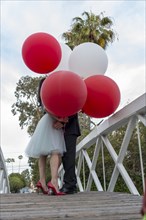 Couple on bridge kissing behind balloons